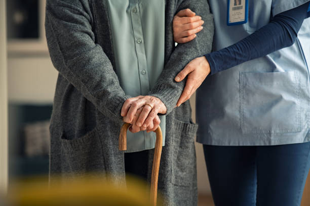 Support worker steadying an older woman walking with a cane at home